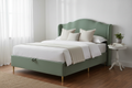Novera Sage Velvet Ottoman Bed with curved headboard and brass legs, bright bedroom